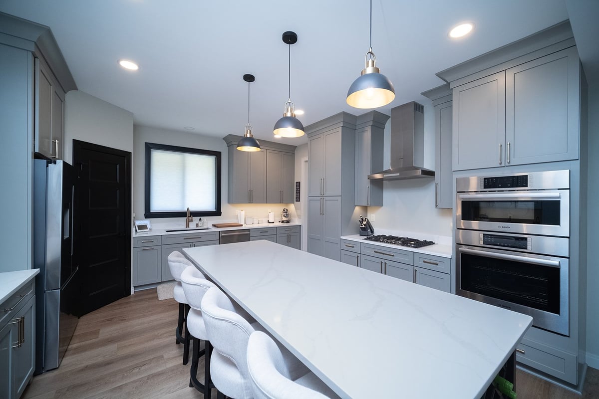 Modern kitchen with gray cabinetry, white marble island, pendant lights, and stainless steel appliances